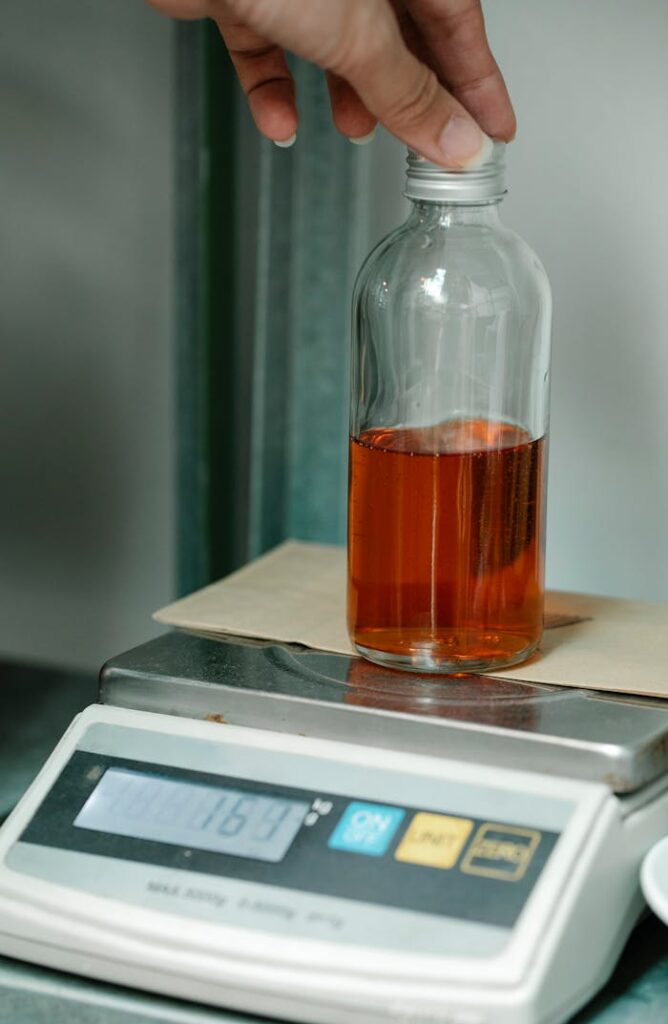 Glass bottle containing liquid being weighed on a digital scale in a laboratory setting.